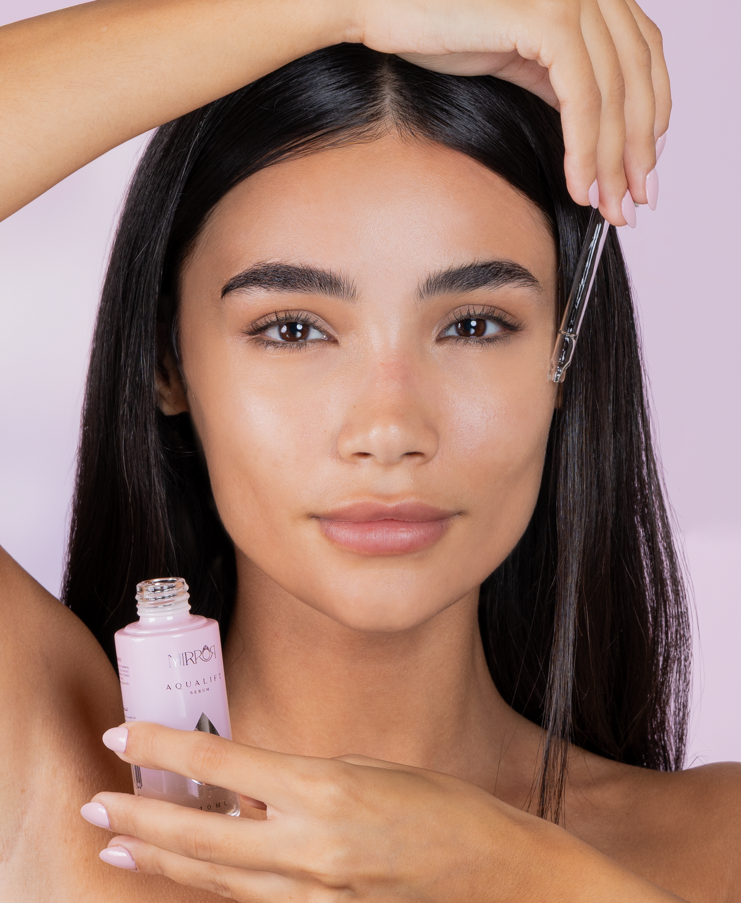 Model applying Mirror Skin Aqualift Hydrating Serum with a dropper on glowing skin against a pastel background.