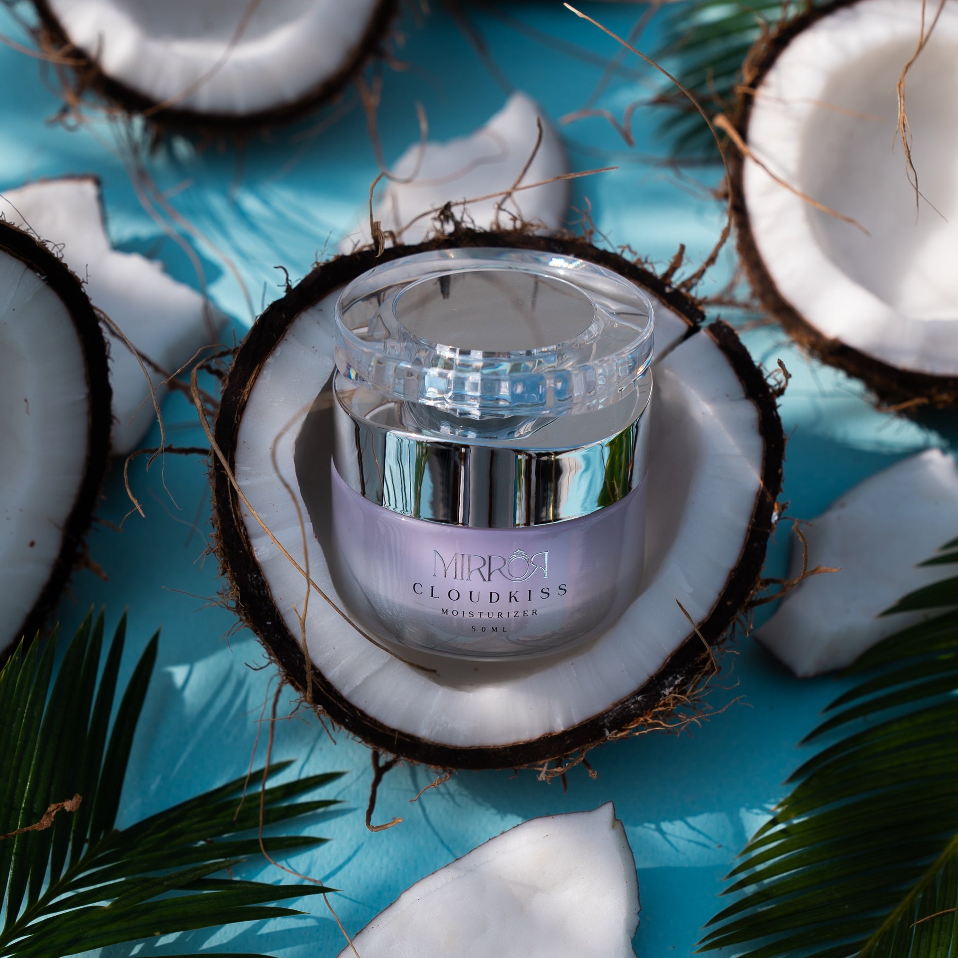 Cloud Kiss moisturizer jar surrounded by coconut and palm leaves.