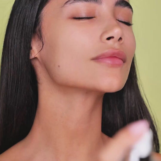 Model applying Mirror Skin Risetone Toner with a cotton pad on her cheek.